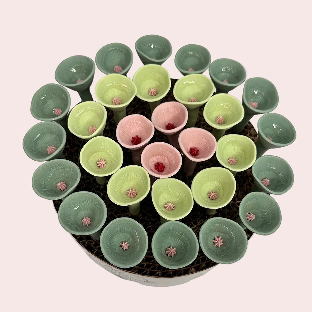 Circular arrangement of small ceramic cups with green, pink, and red contents on a white background